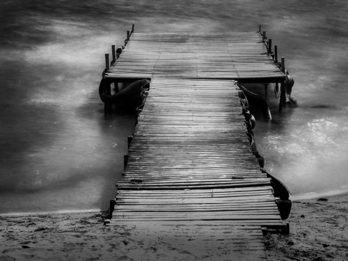 Imagem em preto e branco de uma pequena ponte de madeira sobre o rio
